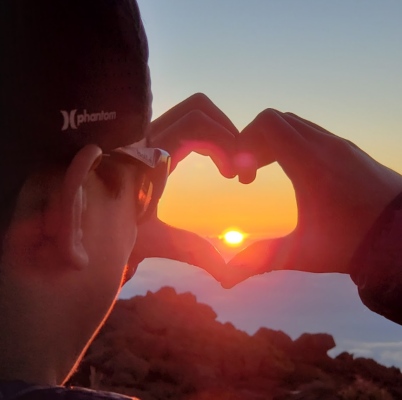 Man making a heart sign with his hands around the sunset